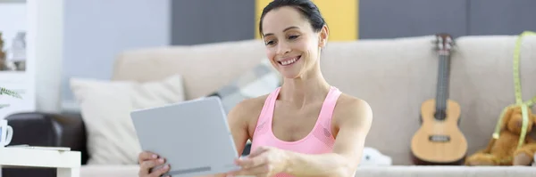 Mulher em sportswear sentado no tapete de ginástica e segurando tablet nas mãos — Fotografia de Stock