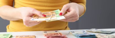 Masada oturan ve elinde avroluk nakit para tutan bir kadın.