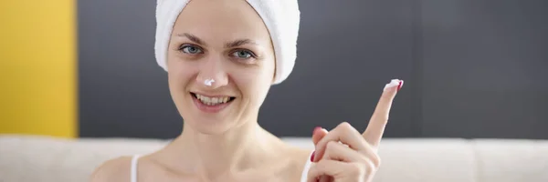 Młoda kobieta z ręcznikiem na włosach nakłada krem ochronny na twarz — Zdjęcie stockowe