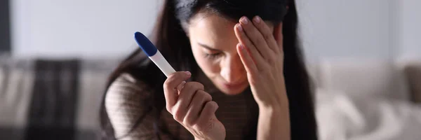 Sad woman sitting on couch and holding pregnancy test closeup