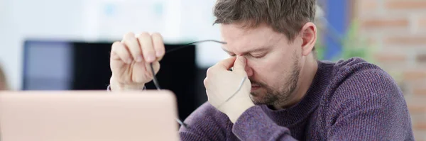 Tired man siting in front of laptop screen and holding glasses in hands — Stock Photo, Image