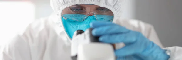 Lekarz w kombinezonie ochronnym i okularach patrzy przez mikroskop — Zdjęcie stockowe