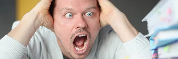 Dumbfounded man holds his head and looks at the stack of folders — Stock Photo, Image