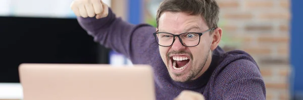 Hombre enojado con gafas ondea su puño en el monitor del ordenador portátil —  Fotos de Stock
