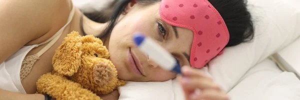 Jovem deitada na cama com termômetro na mão — Fotografia de Stock