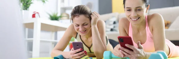 휴대 전화를 가지고 체조를 하고 있는 매트 위에 누워 있는 스포츠 선서를 하는 여자들 — 스톡 사진