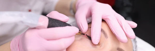 Beauty salon worker applying makeup on visitor eyelid