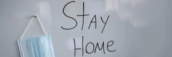 Lettering on white board Stay at home next to protective medical mask