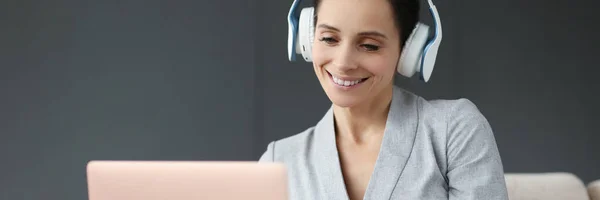 Mulher sorridente em fones de ouvido funciona atrás do laptop — Fotografia de Stock