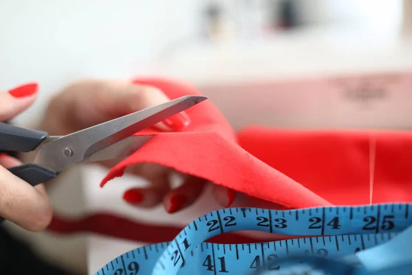 Primer plano de la modista femenina calificada cortando tela roja con tijeras —  Fotos de Stock