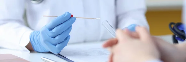 Um médico com luvas de proteção segura um tubo de ensaio na frente de um paciente — Fotografia de Stock