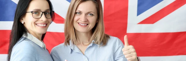 Twee jonge vrouwen met boeken in handen staan tegen de achtergrond van de Britse vlag — Stockfoto