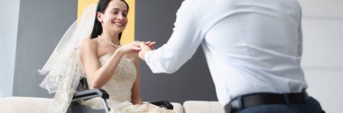 Damat tekerlekli sandalyedeki gelinin parmağına yüzük takıyor.