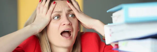 Woman holding her head and is surprised in front of many folders on table — Stock Photo, Image