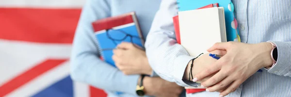 Two students hold notebooks against background of flag of England