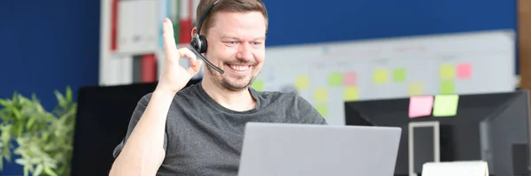 Hombre con auriculares y micrófono en silla de ruedas que muestra el gesto aceptable en el ordenador portátil —  Fotos de Stock