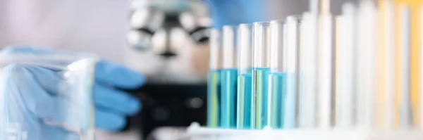 Reagenzgläser mit blauer Flüssigkeit stehen vor dem Hintergrund von Mikroskop-Nahaufnahmen — Stockfoto
