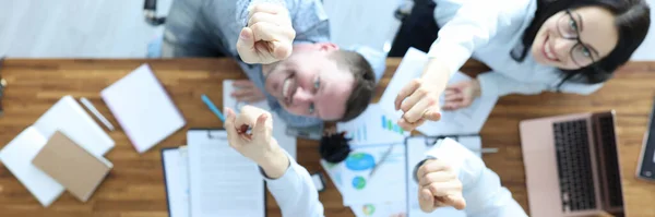 Sorrindo as pessoas na mesa de trabalho com documentos apontar polegares para cima — Fotografia de Stock