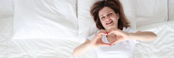 Жінка лежить в ліжку і показує серце своїми руками вид зверху — стокове фото