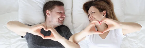 Uomo e donna sdraiati a letto e mostrando il cuore con le mani vista dall'alto — Foto Stock