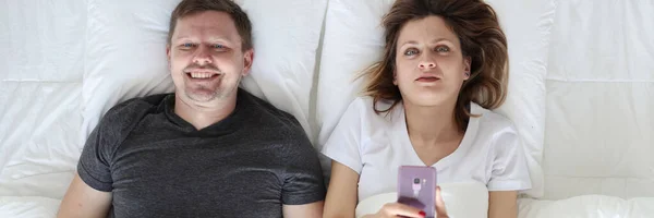 Fiatal férfi és nő fekszik az ágyban, és a kezében telefon és joystick felső nézet — Stock Fotó