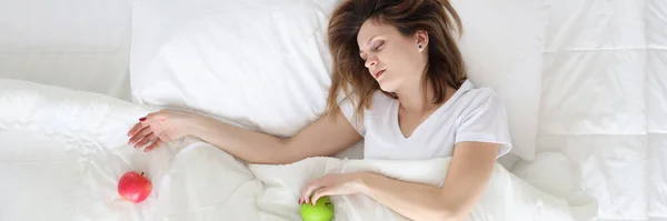 Young woman sleeping in bed with apples in her hands top view — Stockfoto