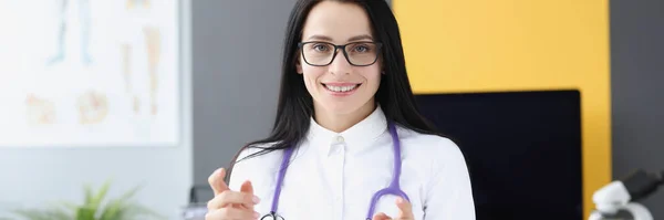 Médica sorridente de casaco branco e estetoscópio em consultório médico — Fotografia de Stock