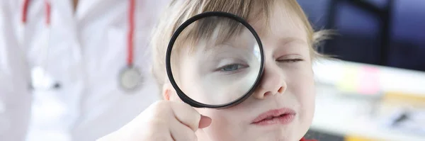 Little girl looks through magnifying glass in background is doctor — Zdjęcie stockowe