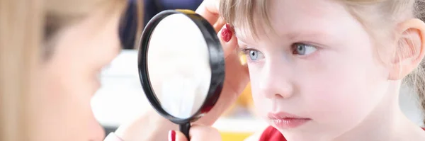 Doctor examining eye of little girl using magnifying glass