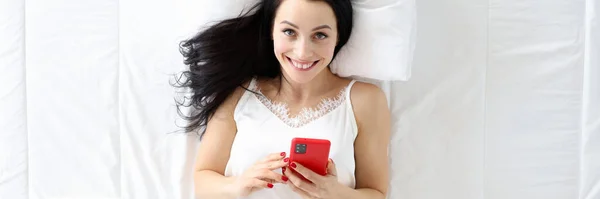 Jonge vrouw liggend in bed met telefoon bovenaanzicht — Stockfoto