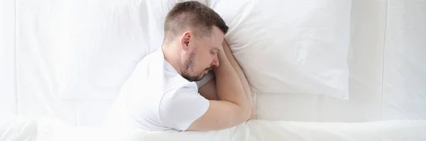 Молодой человек мирно спит на большой белой кровати — стоковое фото