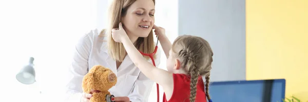 Little girl putting stethoscope on to doctor pediatrician in clinic — Stock Photo, Image