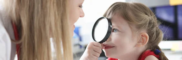 Klein meisje op zoek naar kinderarts arts met vergrootglas in kliniek — Stockfoto