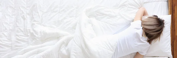 Жінка лежить на білому ліжку і тримає пляшку з алкоголем в руці — стокове фото