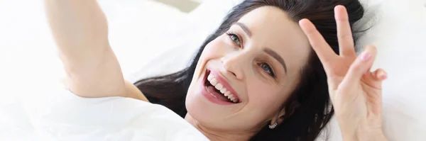 Retrato de jovem sorridente na cama branca tirando selfie no smartphone — Fotografia de Stock