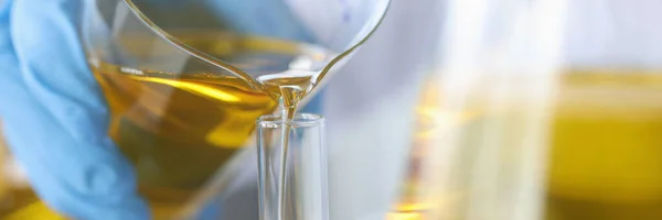 Scientist pours clear golden liquid into glass flask — Stock Photo, Image