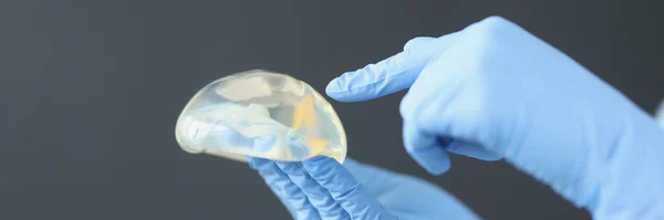 Les mains gantées tiennent l'implant mammaire en silicone — Photo