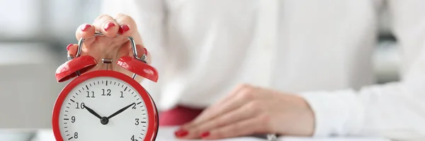 Mujer sentada a la mesa con libro y haciendo clic en primer plano del despertador — Foto de Stock