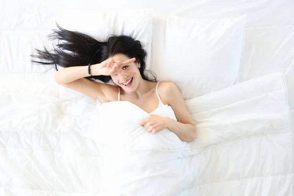 Glimlachende jonge vrouw wakker in de ochtend na een goede nachtrust in wit comfortabel bed bovenaanzicht — Stockfoto