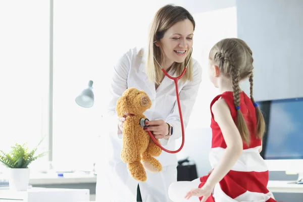 Le pédiatre montre à la petite fille comment utiliser le stéthoscope en utilisant le jouet comme exemple — Photo