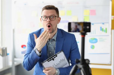 Sürpriz iş koçu cep telefonu kamerasının önünde elinde çizelgelerle dokümanları tutuyor.