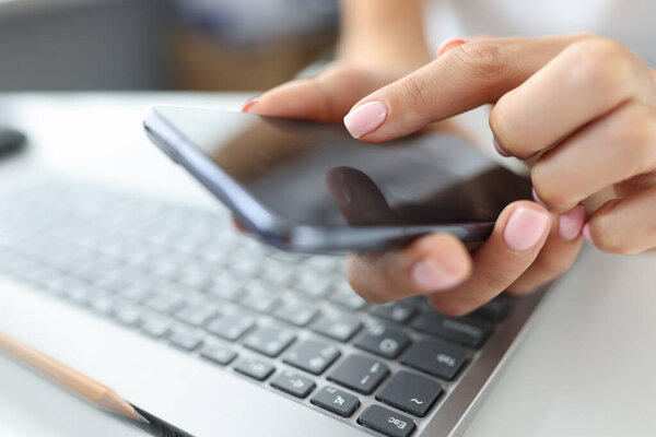 Girl presses finger on screen of smartphone on table is laptop