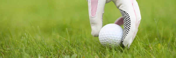 Egy kéz a kesztyűben golflabdát tesz a fűre. — Stock Fotó