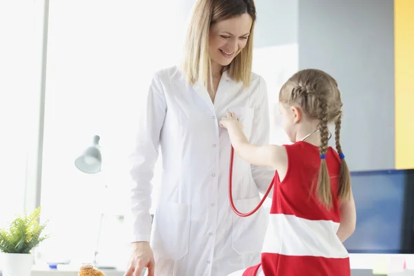 Doktorn kommunicerar med en liten flicka som håller stetoskop. — Stockfoto