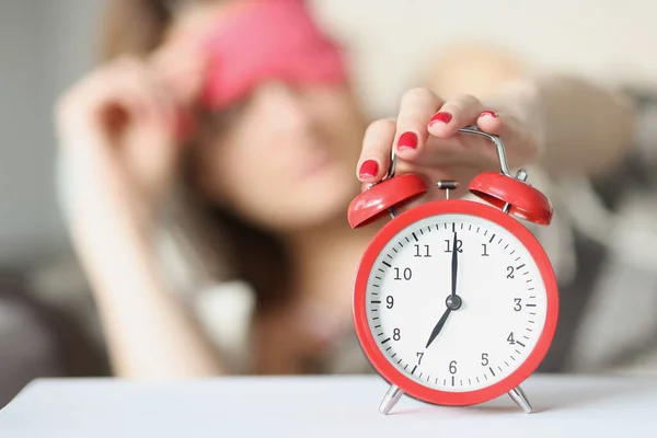 Mujer somnolienta alcanza el despertador rojo a las siete de la mañana —  Fotos de Stock