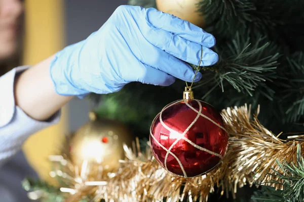 Frau in Schutzhandschuhen hängt Silvesterball am Weihnachtsbaum — Stockfoto