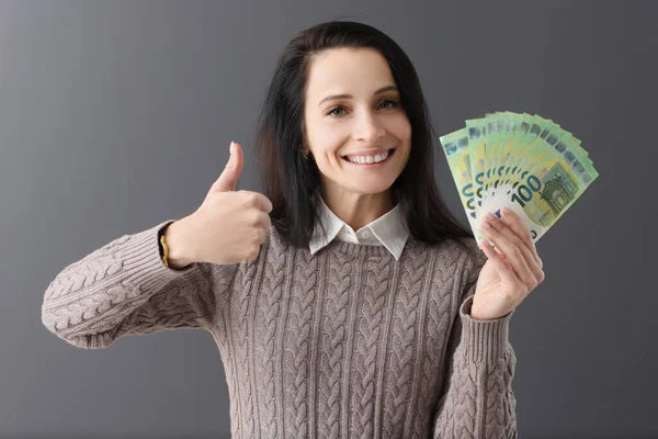 Mujer sonriente sostiene pulgares hacia arriba y billetes de cien euros —  Fotos de Stock