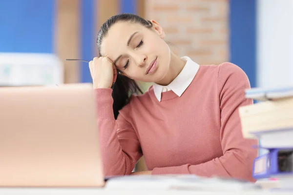 Zmęczona młoda kobieta siedzi w miejscu pracy z zamkniętymi oczami — Zdjęcie stockowe