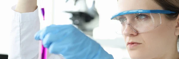 Mujer química en gafas protectoras que gotea líquido rosa en el tubo de ensayo — Foto de Stock