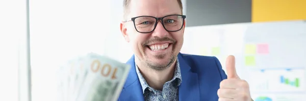 Podnikatel drží dolary v rukou a ukazuje palec nahoru — Stock fotografie